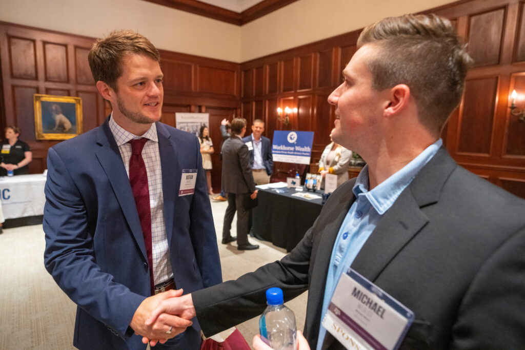 Two business professionals shaking hands in a career fair setting.  