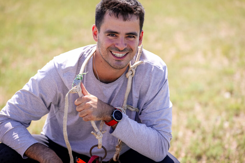 A man in a long sleeve shirt smiles while sitting in a grassy field.