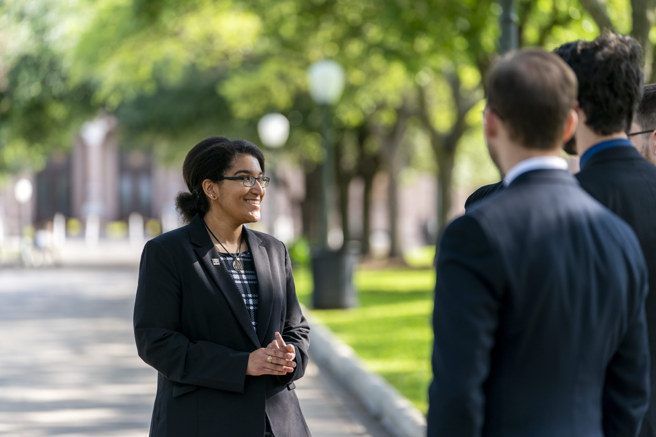 A woman and men, dressed in suits, are talking in a park surrounded by trees