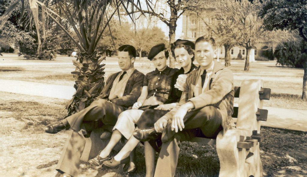 historical shot of four people sitting on a bench outside
