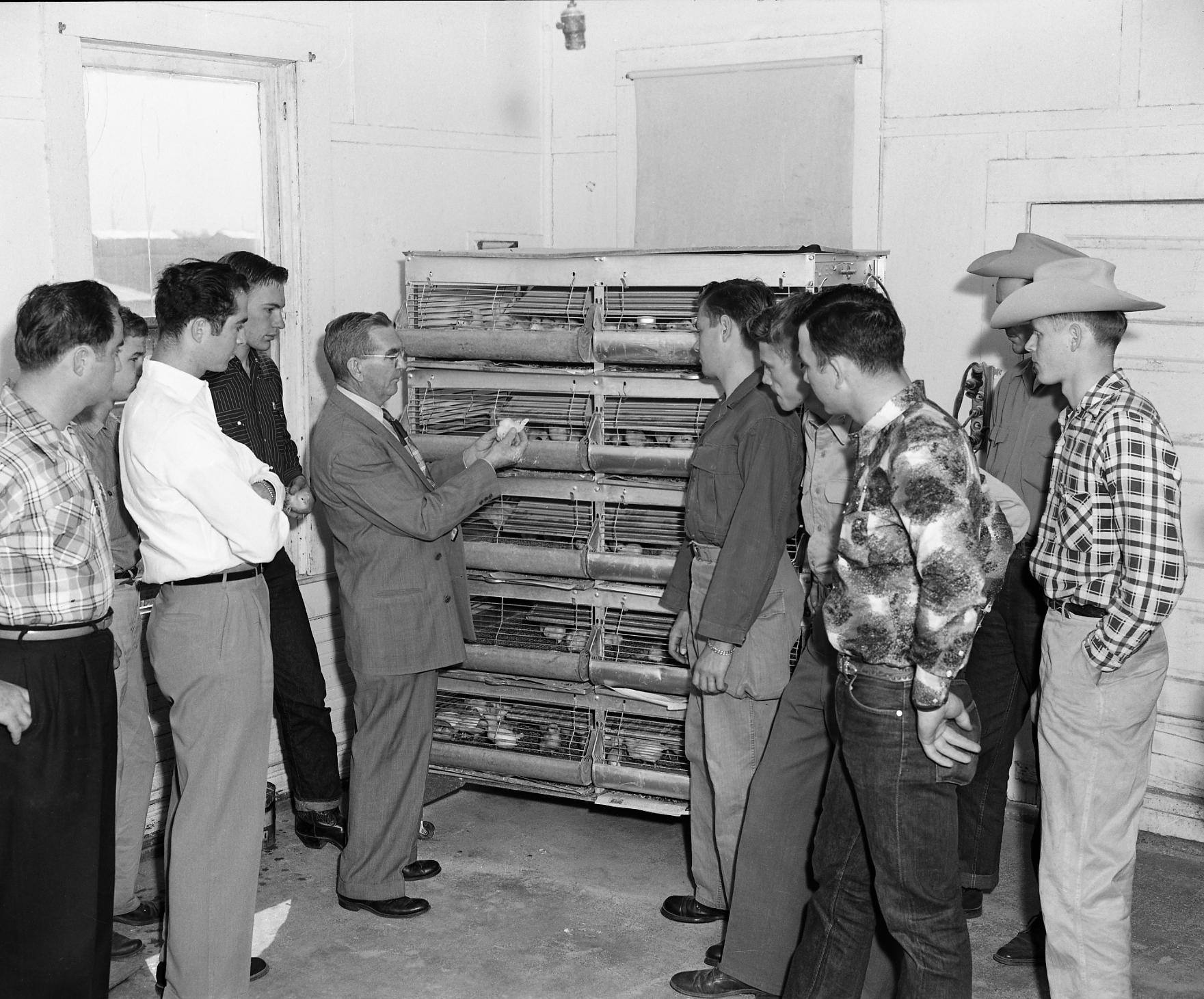 Old black and white picture of a professor demonstrating how a cotton mill works to students