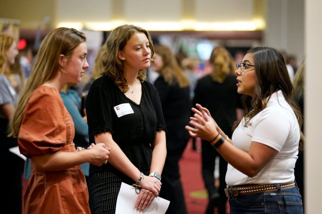 Two students listening to a woman talk at a career fair