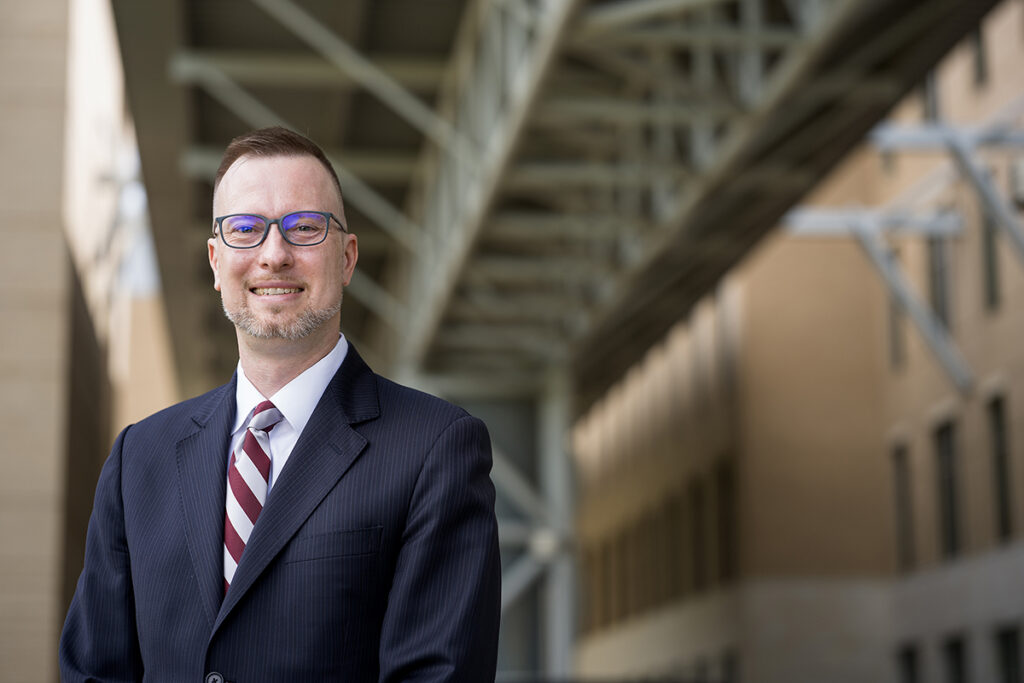 Simon Somogyi, Ph.D. He is wearing a white shirt with a maroon and silver stripped tie and a blue suit jacket