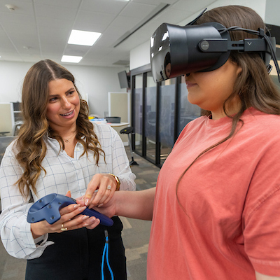 a female student guiding another female student who is using a VR headset