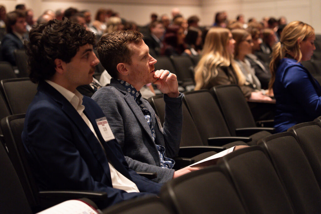 two male students in business attire in the foreground of an auditorium full of students